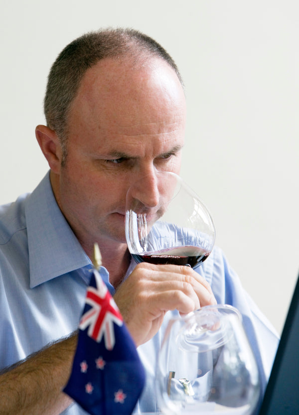 Daniel Schwarzenbach tasting a glass of red wine.  In front of him there is a New Zealand flag.   