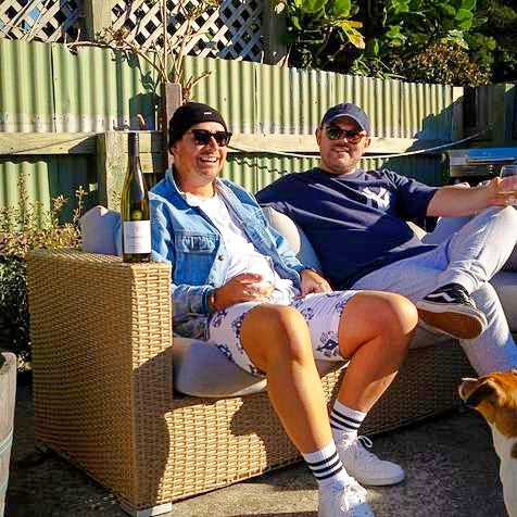 Sam Waghorn of Wag & Co and his partner relaxing on an outside couch with a glass of wine.  On the armrest there is a bottle of Blackenbrook Pinot Gris. They both look really happy and stylish.