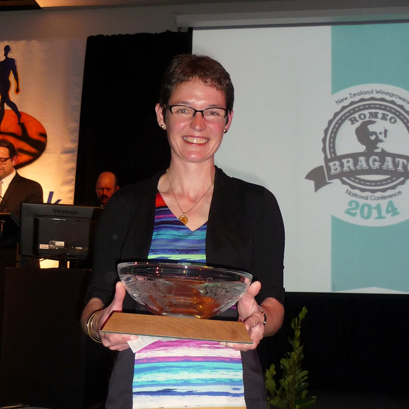 Owner Ursula Schwarzenbach accepting the Trophy for best Pinot Gris at the Bragato Wine Awards 2014.  She is holding the crystal trophy in front of her.  In the background there is a screen displaying the Bragato Wine Awards logo. 