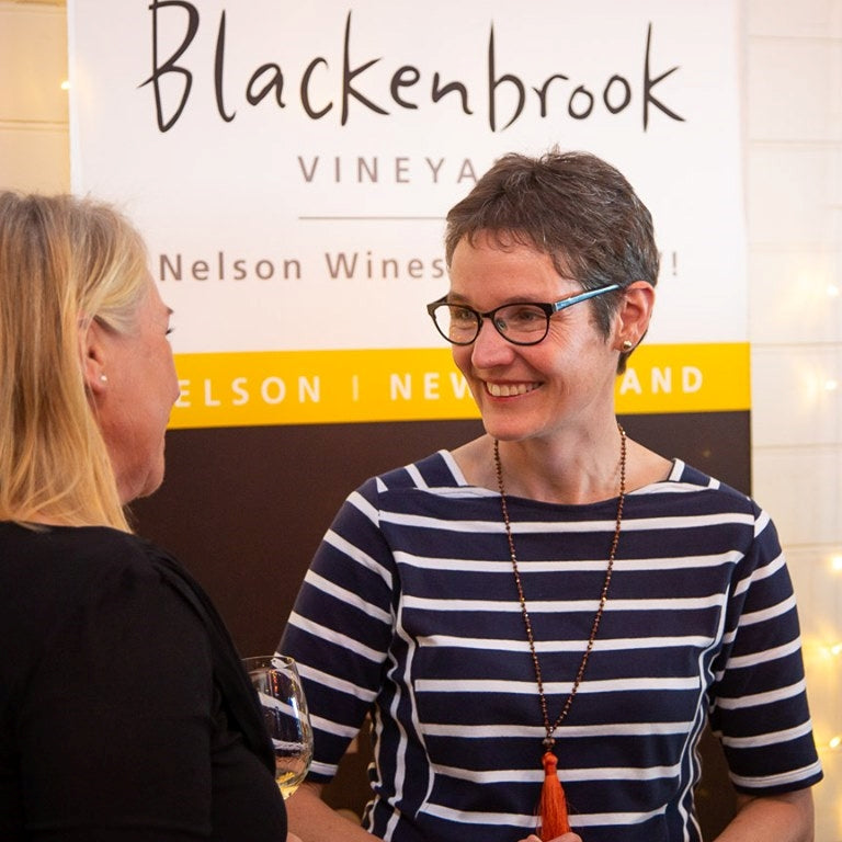 Ursula Schwarzenbach chatting with a customer at a wine tasting.  In the background there is a large Blackenbrook sign. 