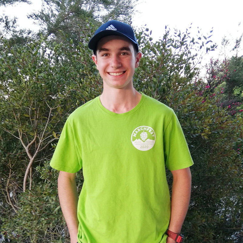 Thomas Schwarzenbach standing in front of a Manuka tree.  He is smiling, wearing a bright green t-shirt and a black cap. 
