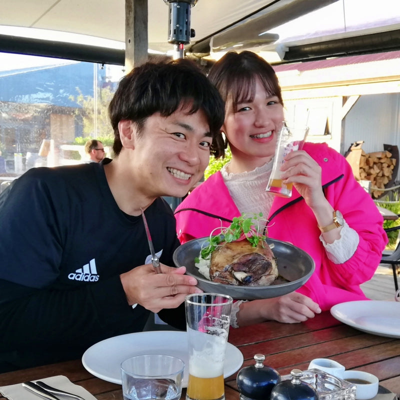 Our Japanese wine importers Yumi Toyama and Masaki Tokunaga enjoying a meal in Mapua.  Both are smiling and Yumi is wearing a bright pink coat.