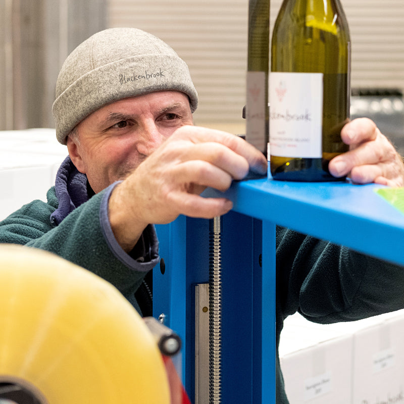 Winemaker Daniel Schwarzenbach holds up a ruler next to a bottle of Blackenbrook wine sitting on a blue shelf in the winery while the new vintage is being bottled.