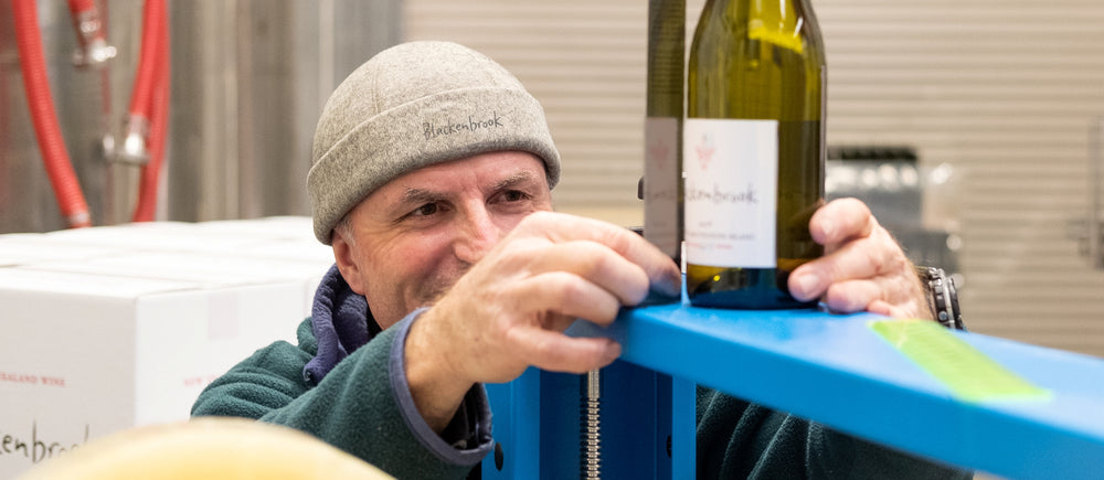 Daniel Schwarzenbach measuring a Blackenbrook wine label on a bottle that sits on a blue stand. He looks very focussed.