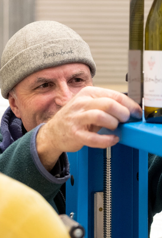 Daniel Schwarzenbach measuring a Blackenbrook wine label on a bottle that sits on a blue stand. He looks very focussed. 
